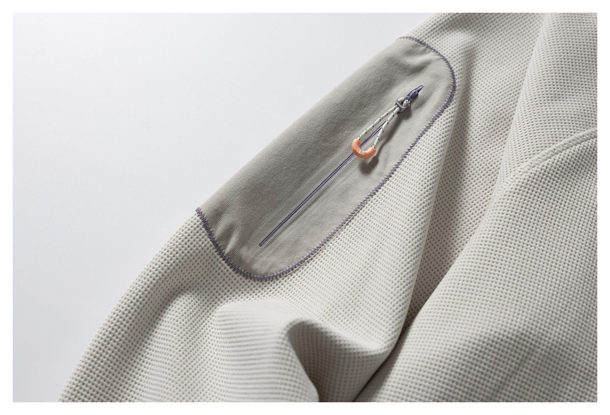 Close-up of an off-white jacket sleeve with a gray zip pocket and contrasting purple stitching.