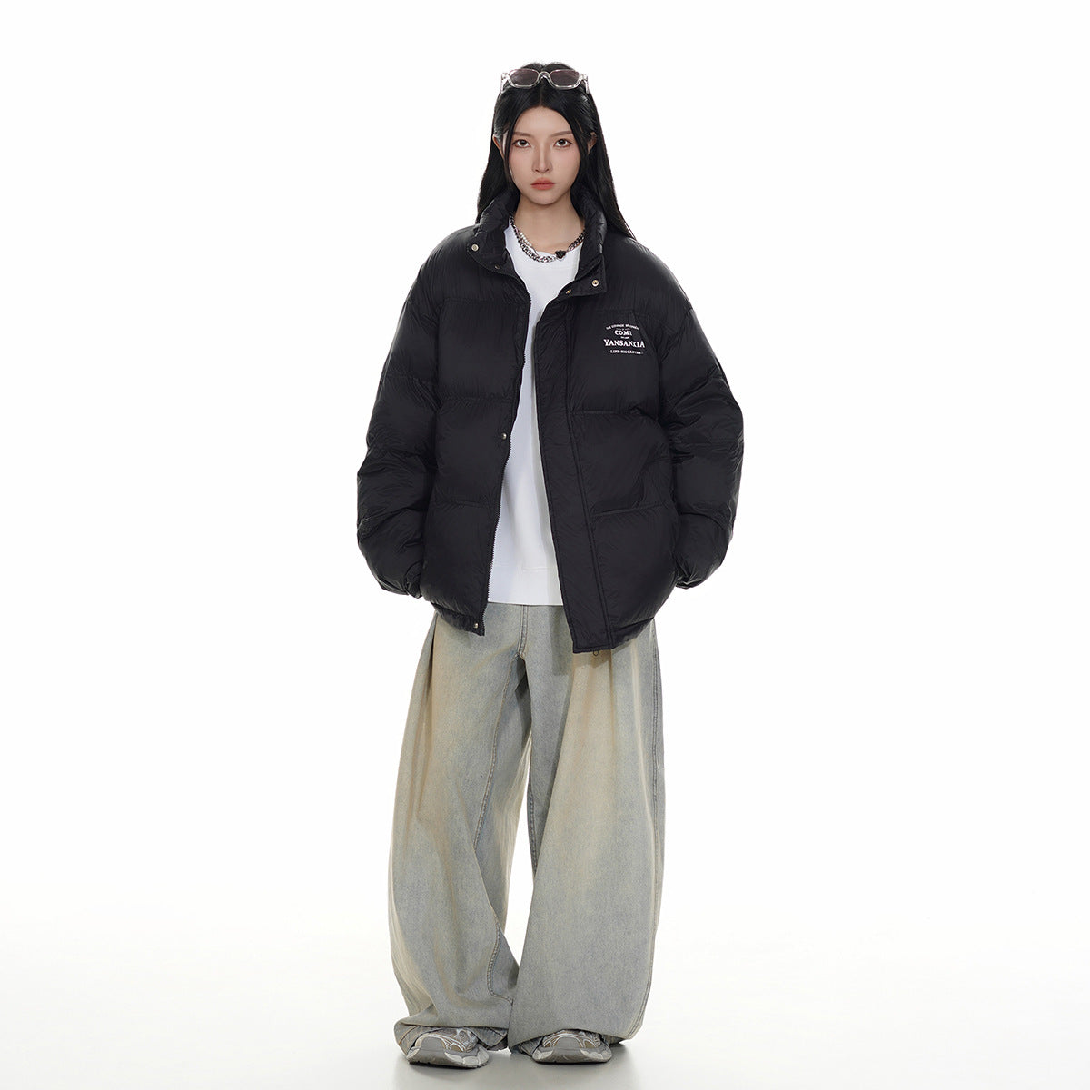 Full-length front view of a model in a black puffer jacket, white top, and loose light-wash jeans.