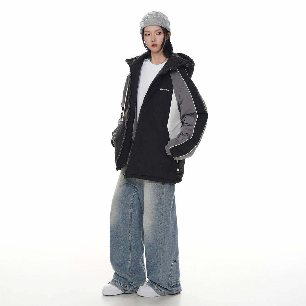 Model wearing a black hooded jacket with gray and white panels and white piping, paired with wide-leg jeans.
