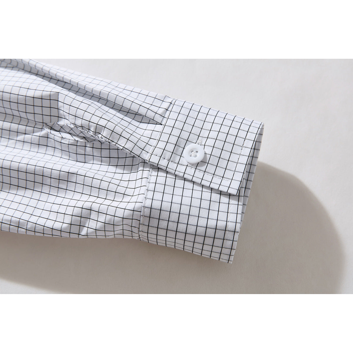 Close-up of the buttoned cuff on a white shirt with a fine black windowpane check.