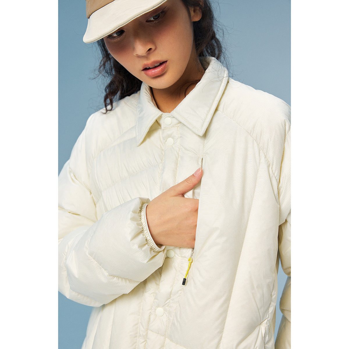 Close-up of a model wearing an off-white quilted jacket with a pointed collar, snaps, and a zip pocket.