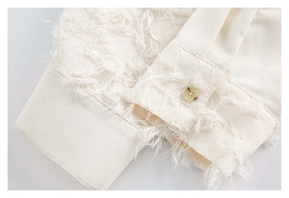 Close-up of an ivory garment cuff with a small button and frayed floral mesh trim.