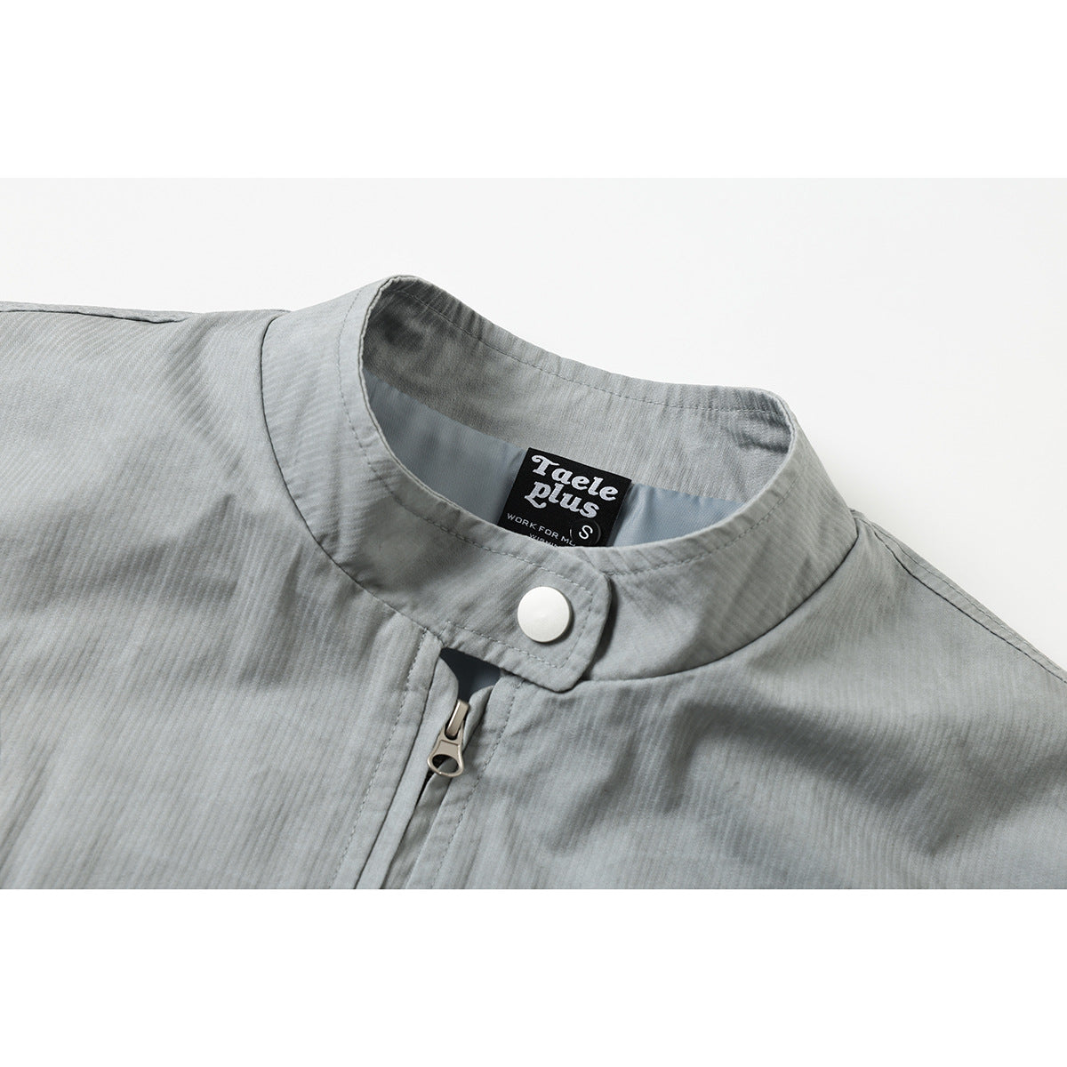 Close-up of a light gray jacket's stand collar, white snap, front zipper, and sewn neck label.