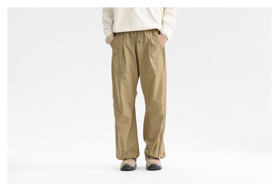 Front view of a model wearing loose khaki drawstring pants with large front pockets.