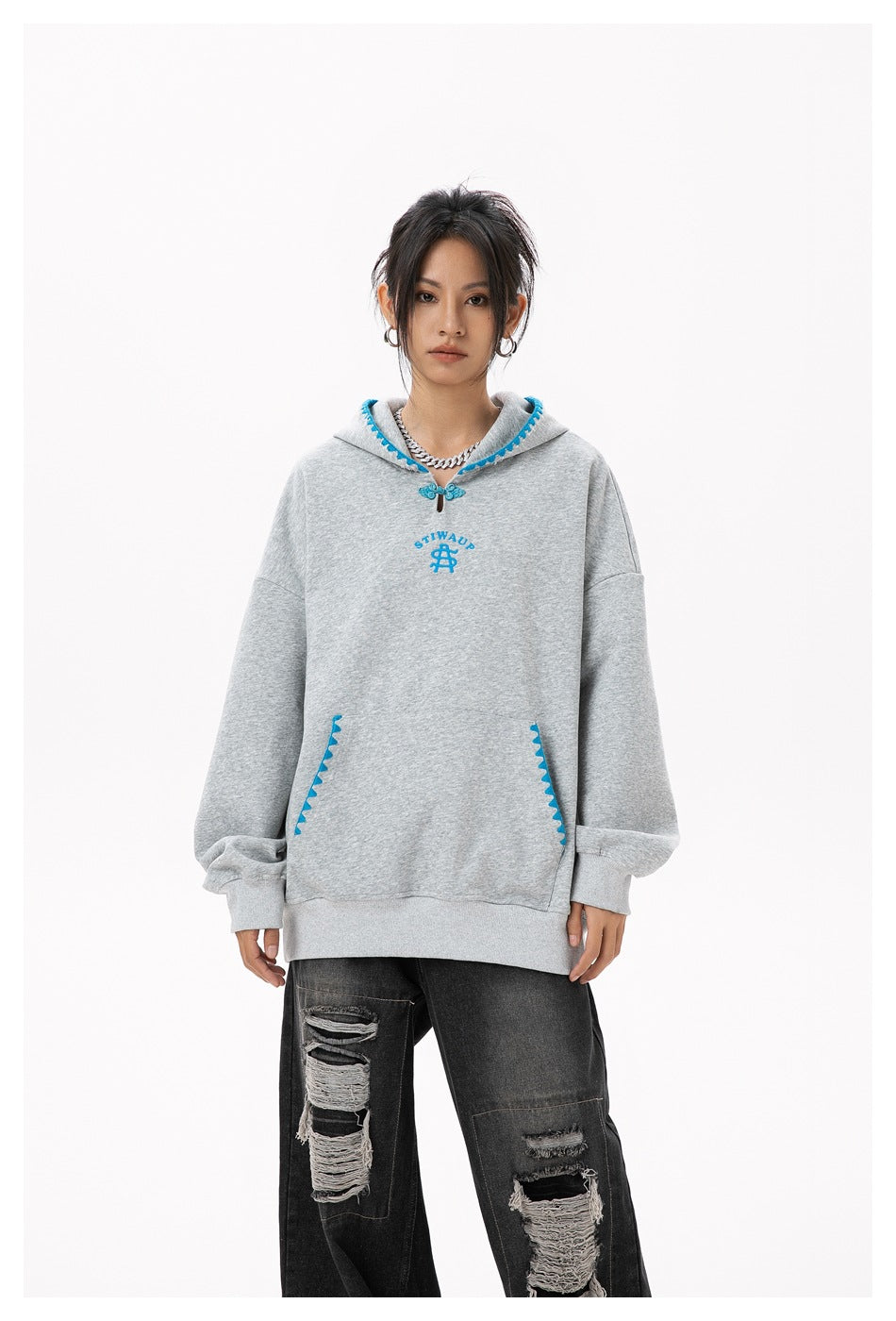 Front view of a model wearing a gray oversized hoodie with blue trim and black distressed jeans.