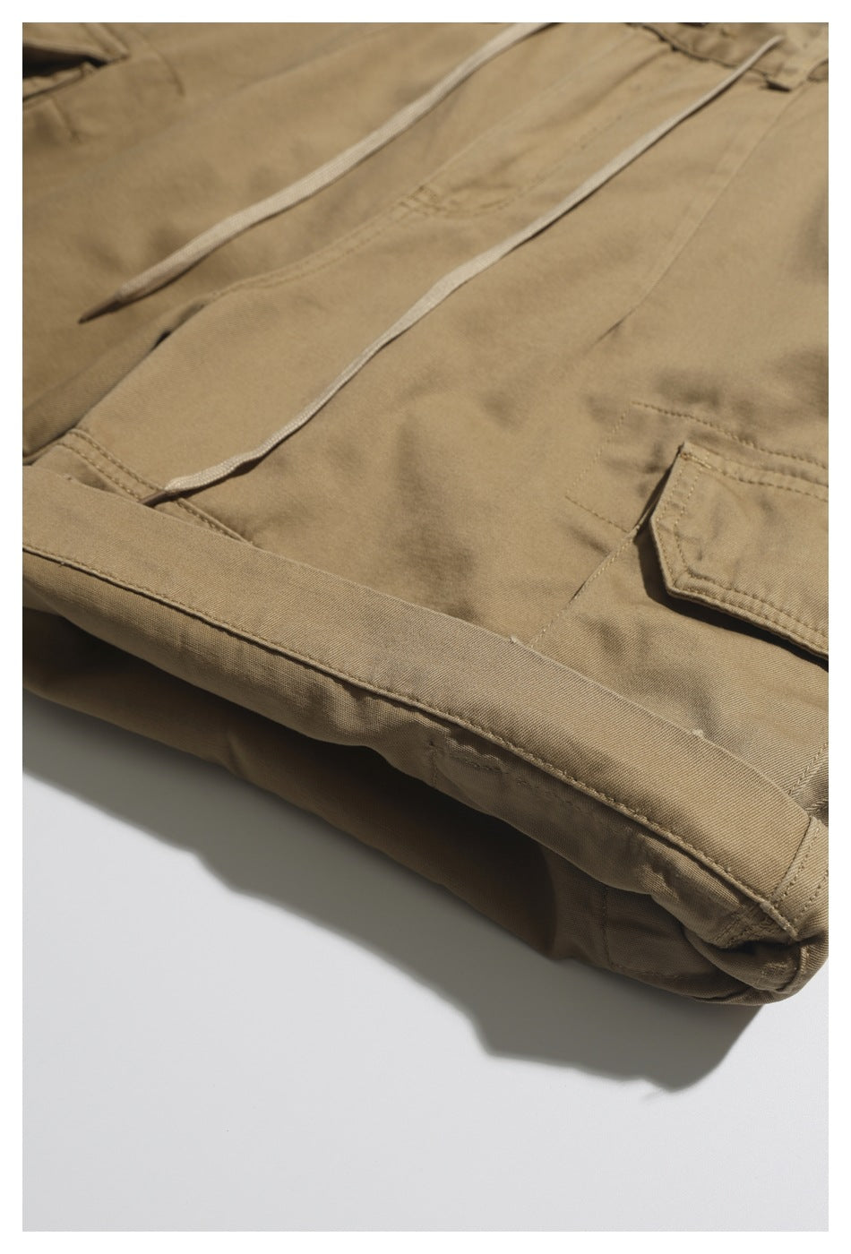 Close-up of khaki trousers with a drawcord waist and a buttoned cargo pocket.