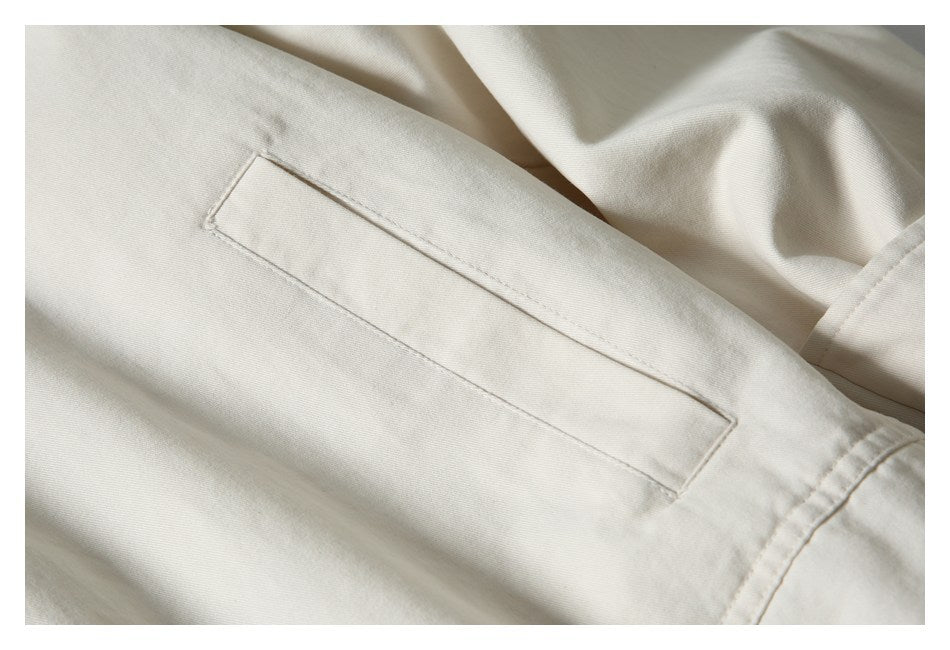 Close-up of a long rectangular stitched pocket on cream jacket fabric.