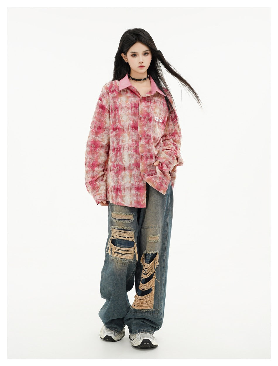 Model wearing a pink tie-dye plaid oversized button-up shirt with ripped wide-leg jeans, front view