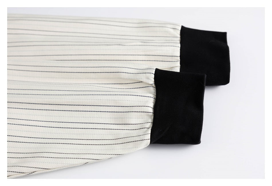 Close-up of cream fabric with fine dark pinstripes and wide black cuffs.