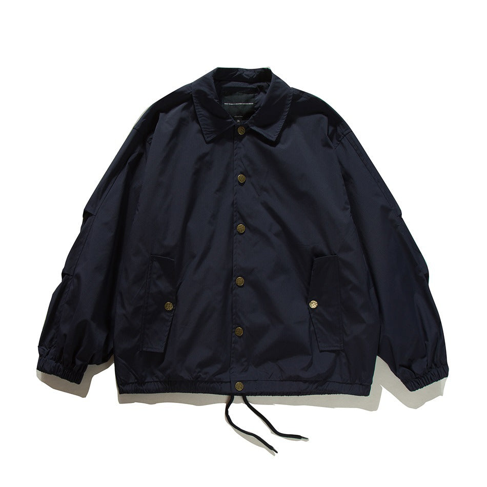 Navy coach-style jacket flat lay, front view with gold buttons, flap pockets, elastic cuffs and drawstring hem