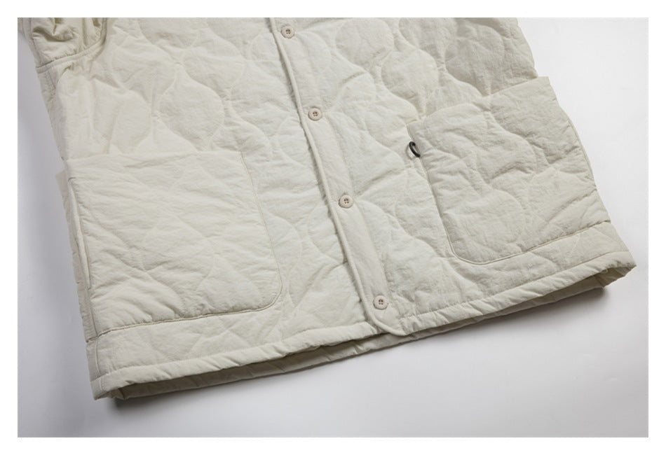 Close-up of the ivory jacket's front buttons, two patch pockets, quilted stitching, and hem.