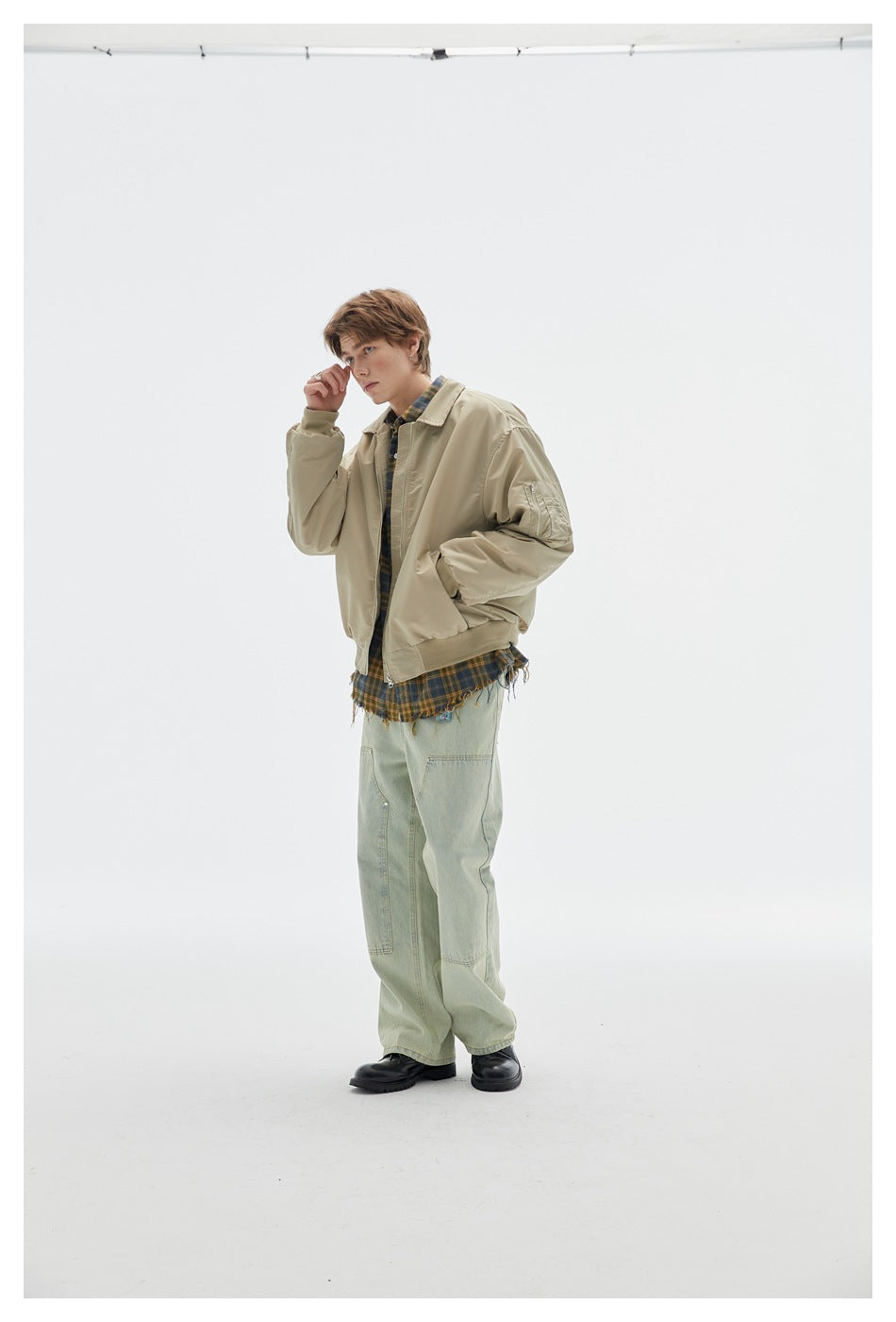 Three-quarter view of a model wearing a beige zip-front jacket with a sleeve pocket and plaid shirt.