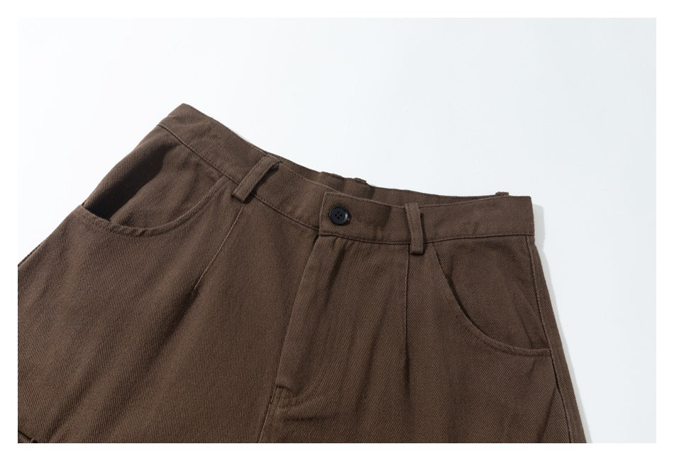 Close-up of brown trousers showing the waistband, button, belt loops, and slanted front pockets.