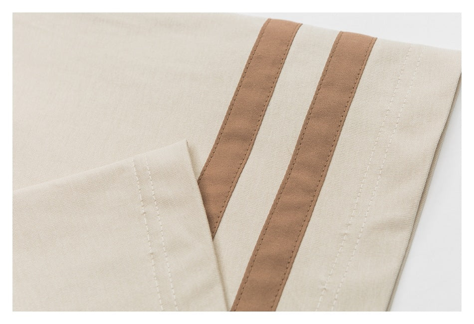 Close-up of a beige T-shirt sleeve with two parallel brown stripes and visible stitching.