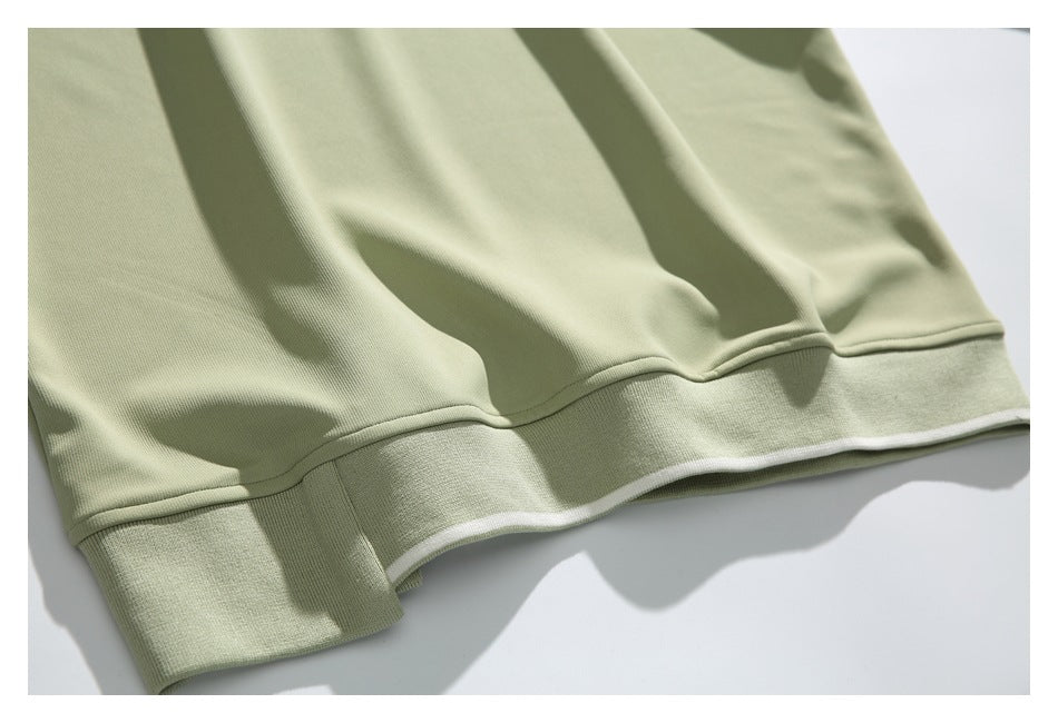 Close-up of the pale sage-green sweatshirt hem and wide ribbed band with a thin white edge.