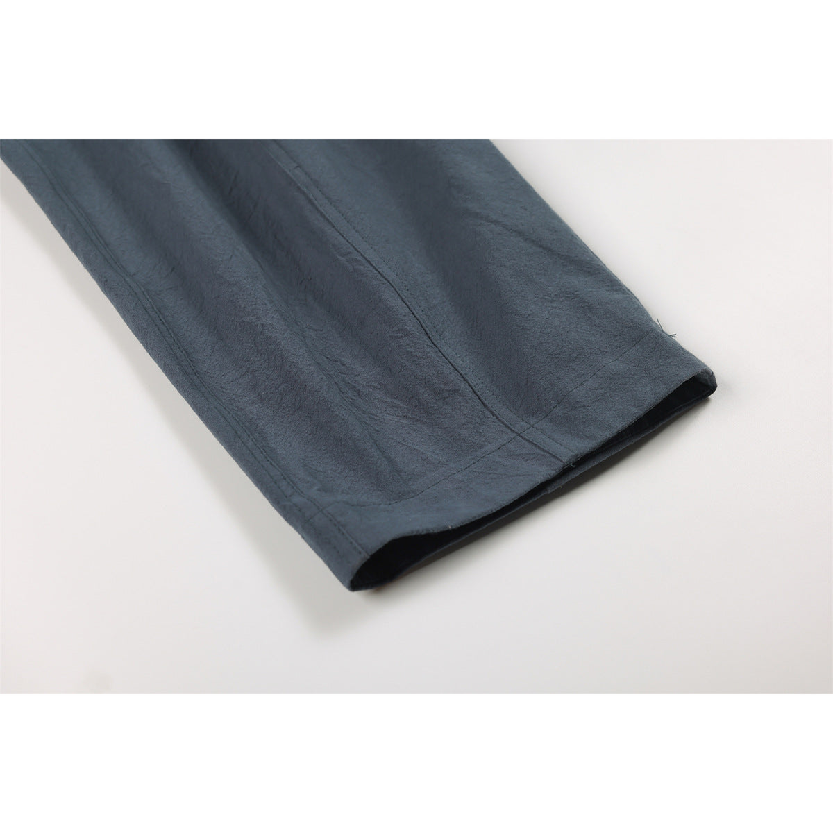 Close-up of the stitched hem and leg of dark slate-blue trousers.