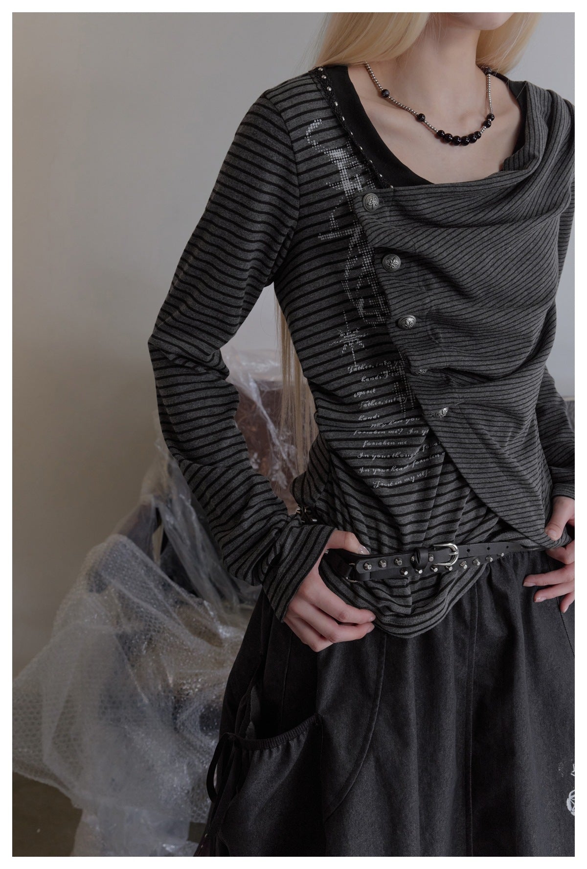Close view of a model wearing a charcoal-and-black striped top with a draped neckline and decorative buttons.