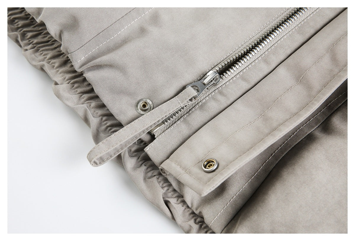 Close-up of a taupe-gray jacket's zipper, snap fasteners, and gathered edge.