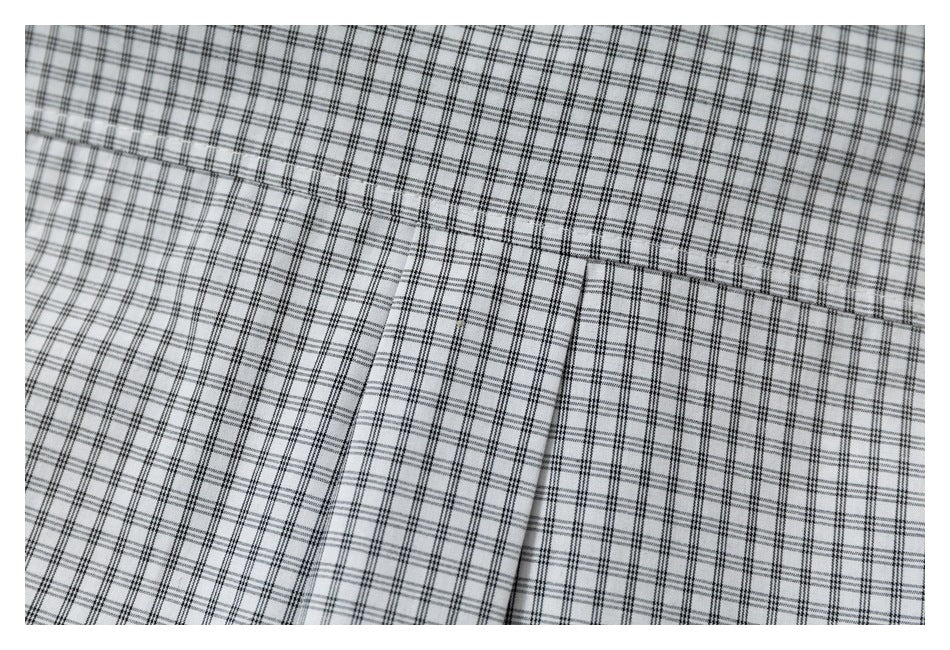Close-up of a black-and-gray checked shirt showing a chest pocket and its stitching.