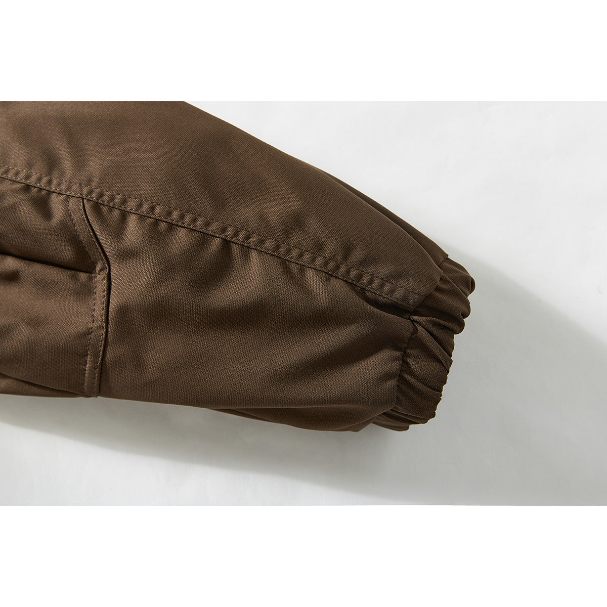 Close-up of a brown jacket sleeve showing stitched panels and an elasticated cuff.