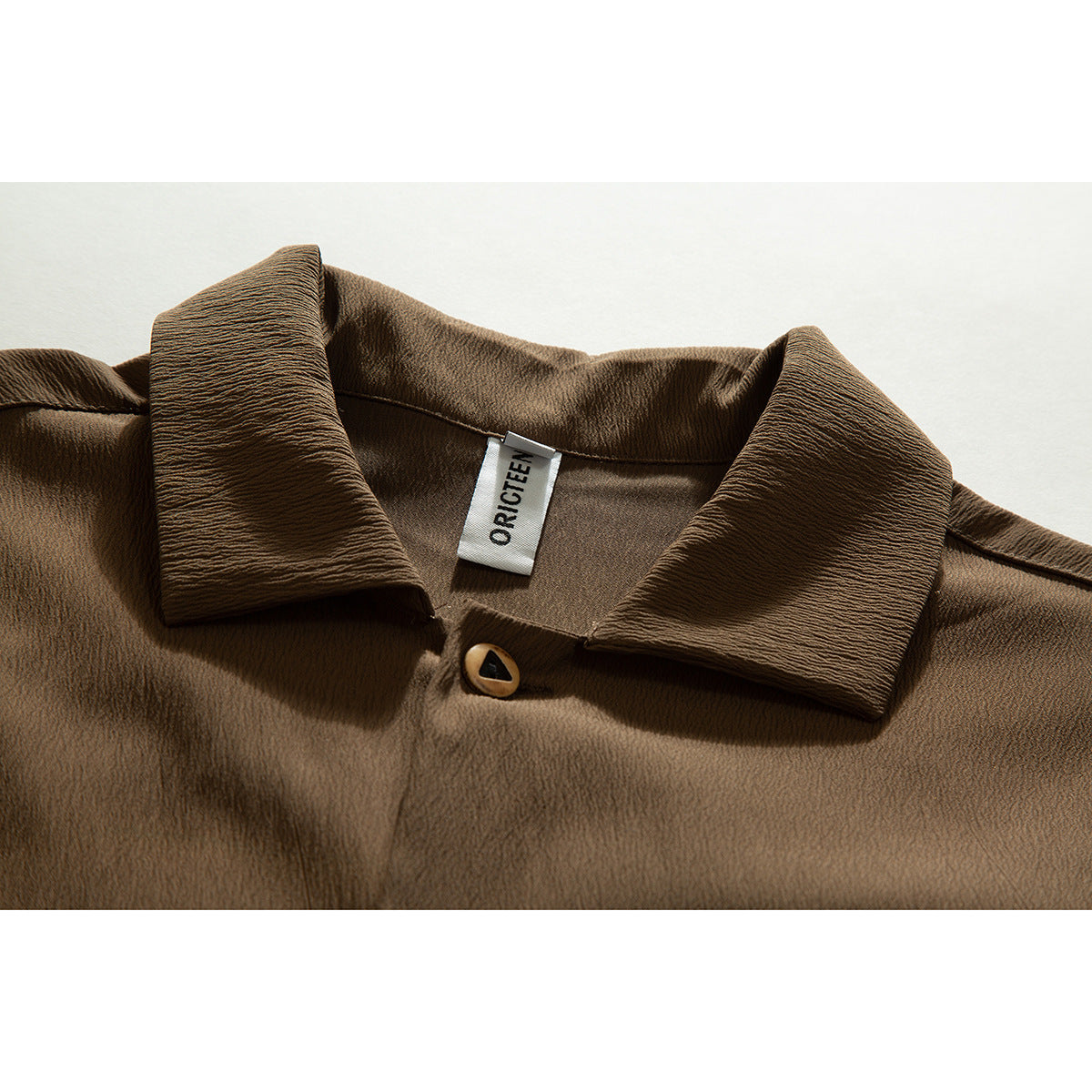 Close-up of a brown shirt collar, top button, and sewn neck label.