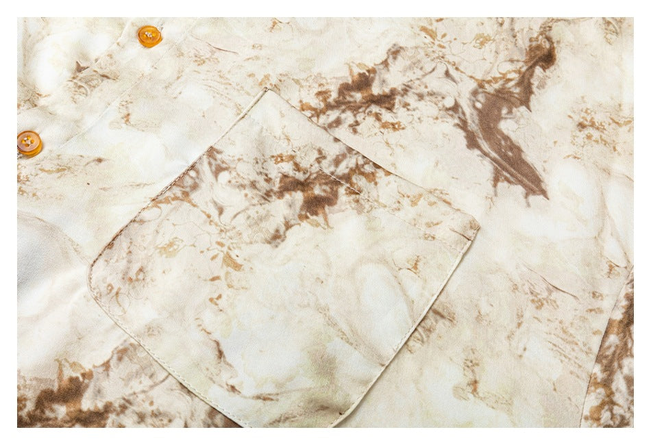 Close-up of a cream shirt with brown abstract print, showing a chest pocket and amber buttons.