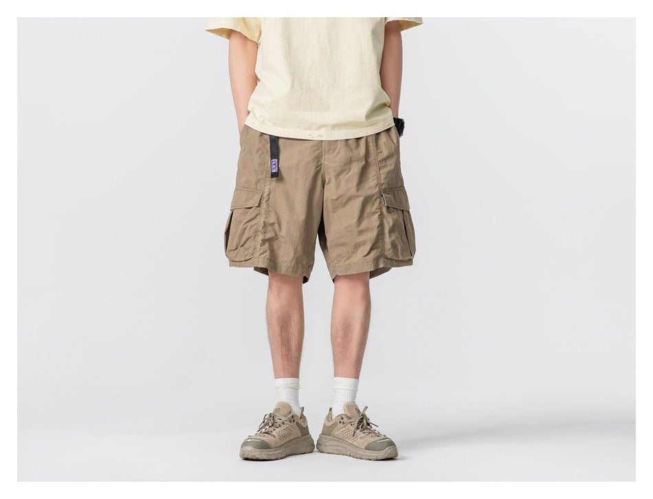 Model wearing brown cargo shorts with belt and thigh pockets, with a cream t-shirt, white socks and tan sneakers