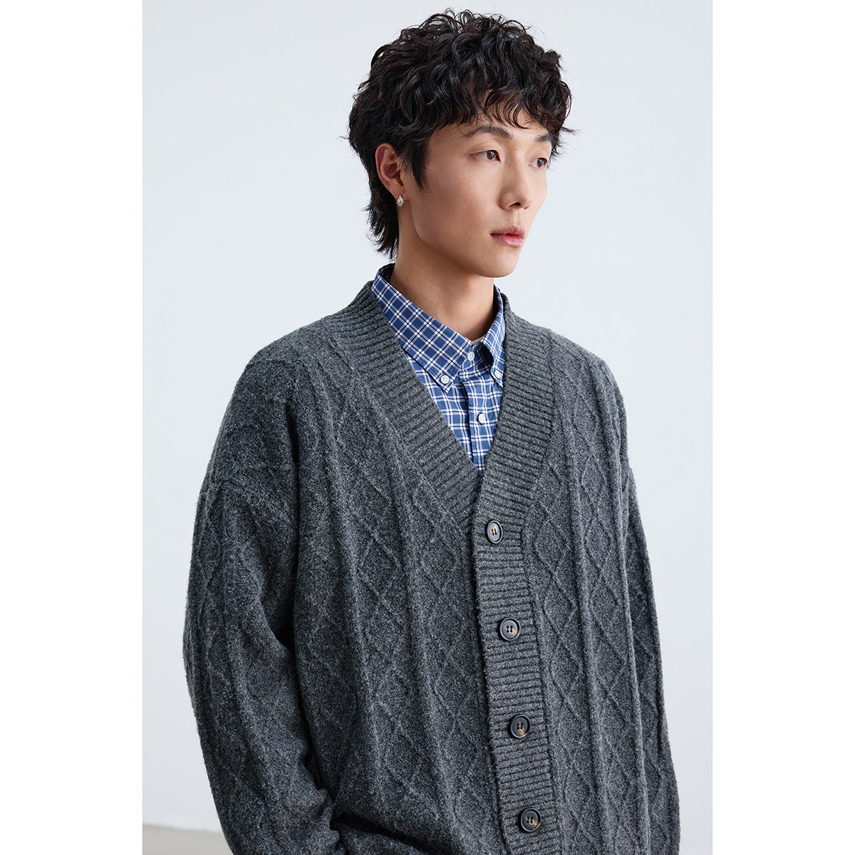 Close view of a model wearing a charcoal diamond-knit cardigan over a blue plaid shirt.
