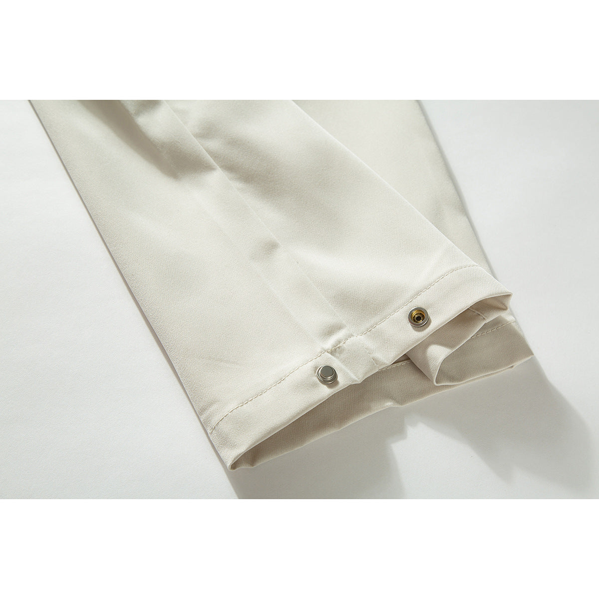 Close-up of a cream trouser cuff with metal snap fasteners.