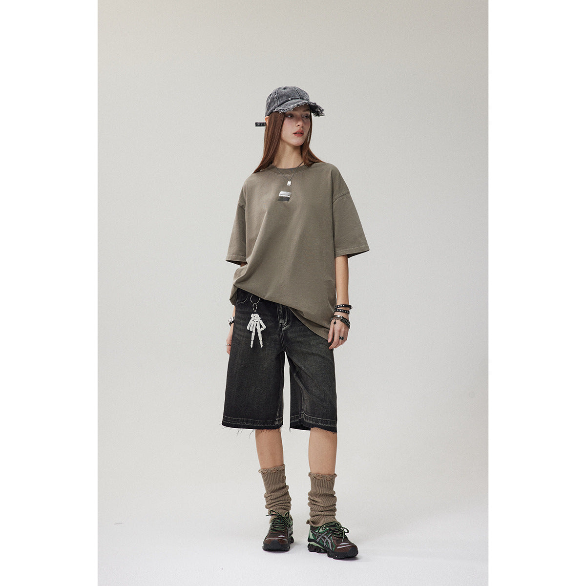 Model wearing an oversized taupe T-shirt with a small chest graphic and black knee-length denim shorts.