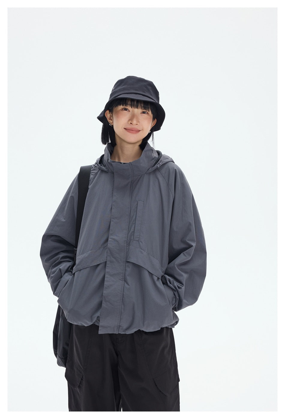Closer view of a model wearing a gray hooded jacket with black pants and a black bucket hat.