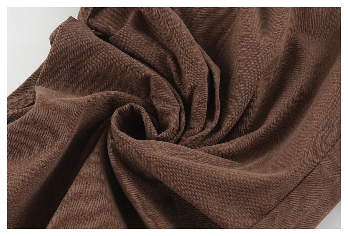 Close-up of brown trouser fabric gathered into folds, showing its woven texture.