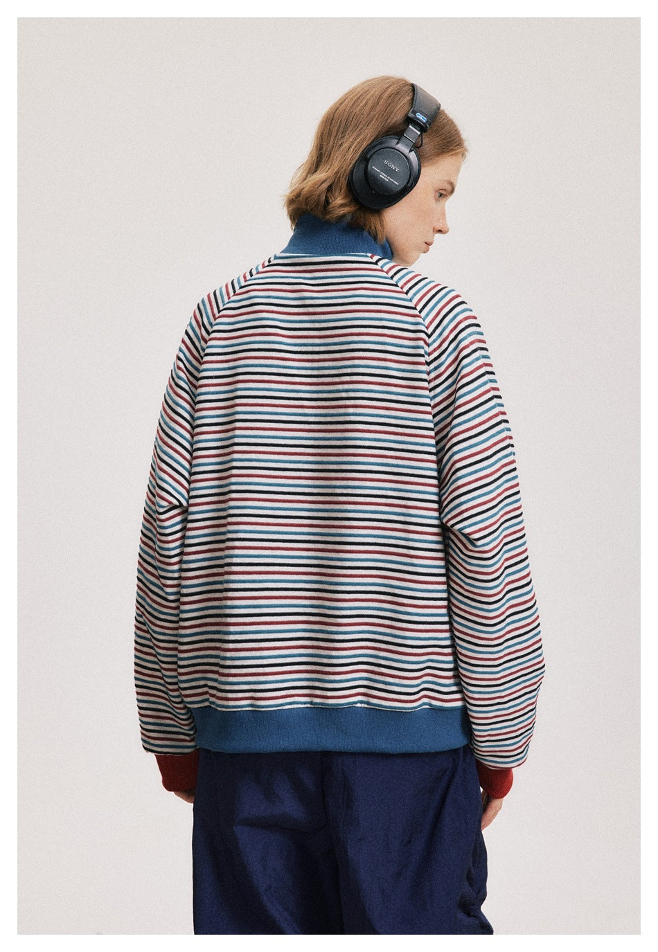 Rear view of a model wearing the striped jacket with a blue collar and hem and red cuffs.