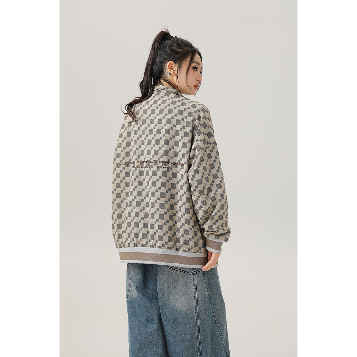 Rear view of a model in an oversized beige-and-charcoal checker jacket with printed text across the back.