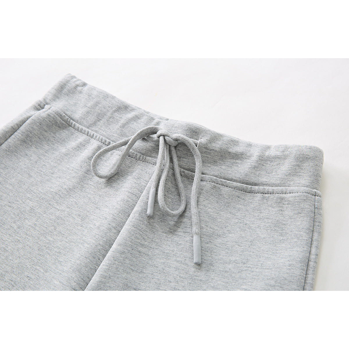 Close-up of light gray shorts showing the elastic waistband, front seam, and tied drawstring.