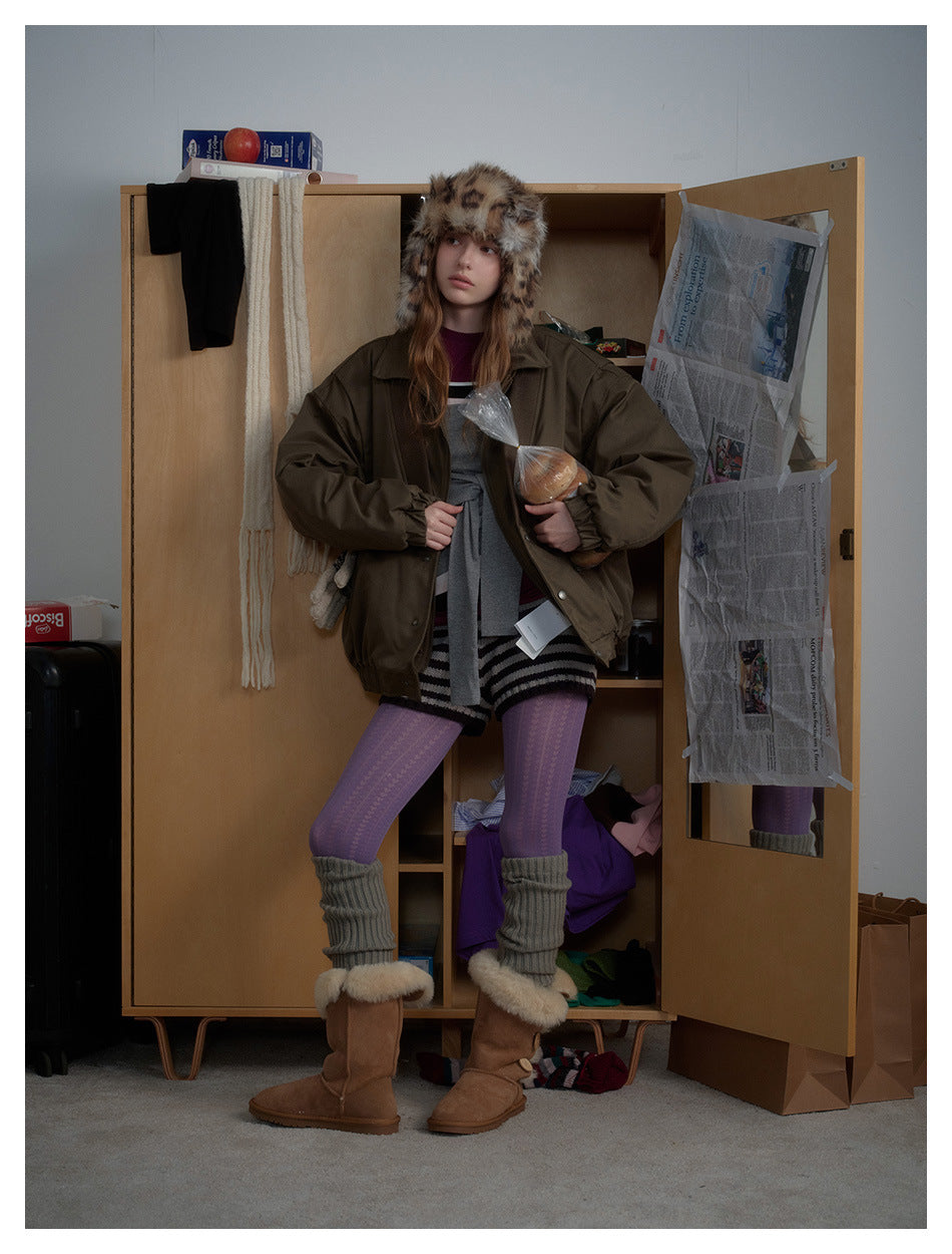 Model wearing an oversized olive jacket, spotted fur hat, purple tights, gray leg warmers and brown boots.