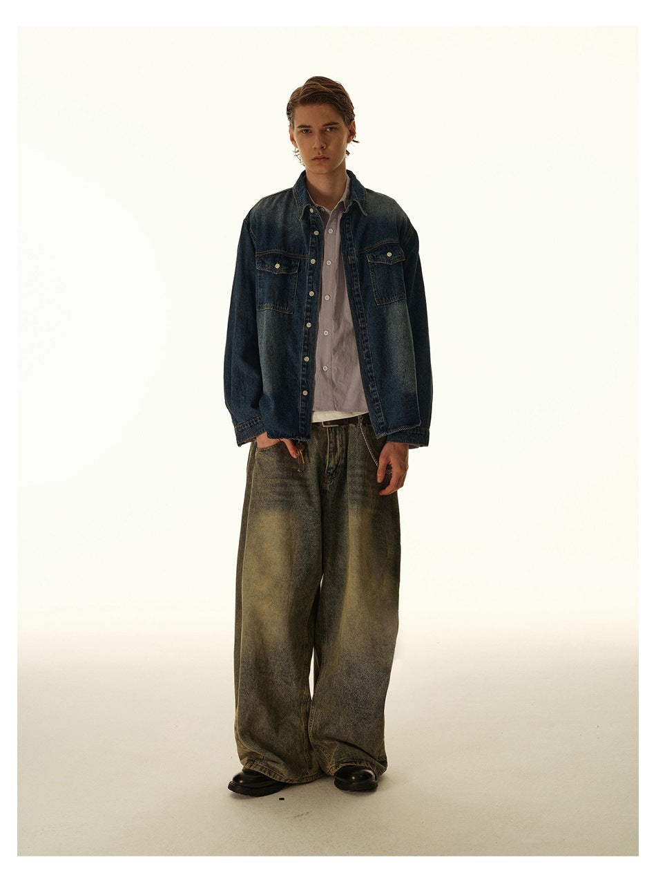 Full-length front view of a man wearing a dark blue denim overshirt with chest pockets and wide faded jeans.
