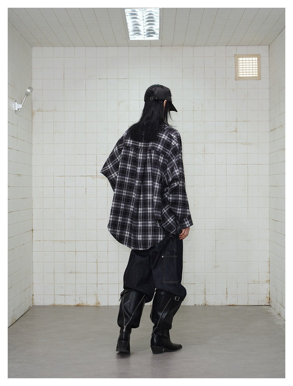 Rear view of a model wearing an oversized black and gray plaid shirt with a curved hem.