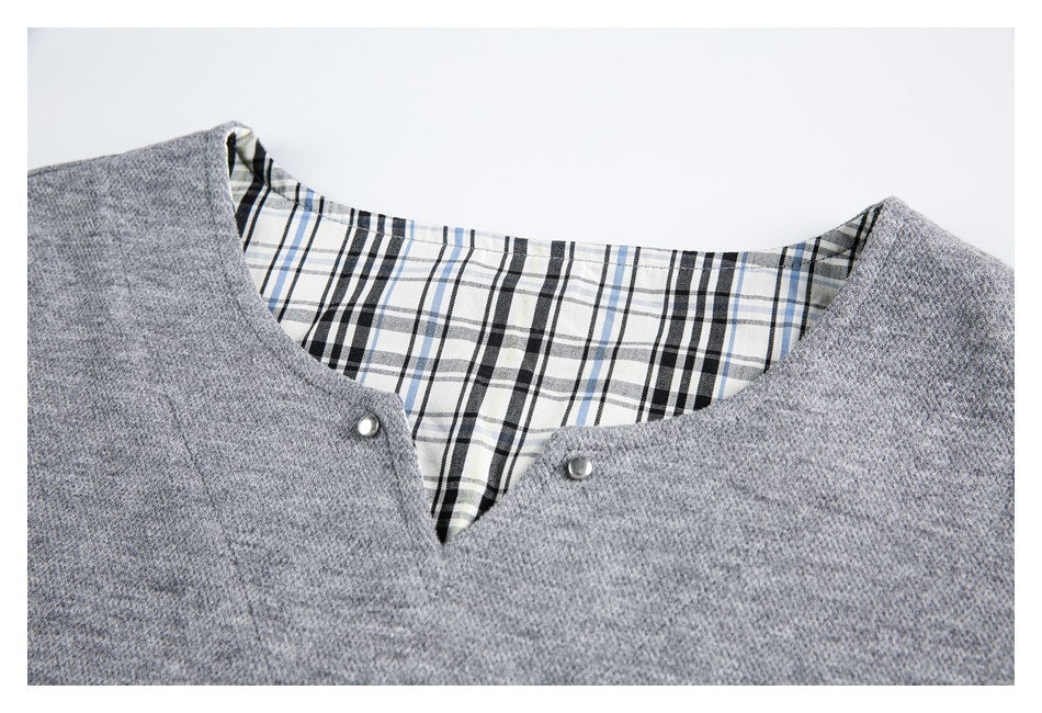 Close-up of a gray garment's V-shaped neckline with two metal snaps and black, white, and blue plaid lining.