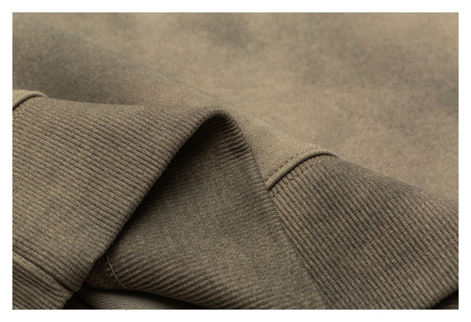 Close-up of taupe-brown garment fabric with a folded ribbed edge and visible stitching.