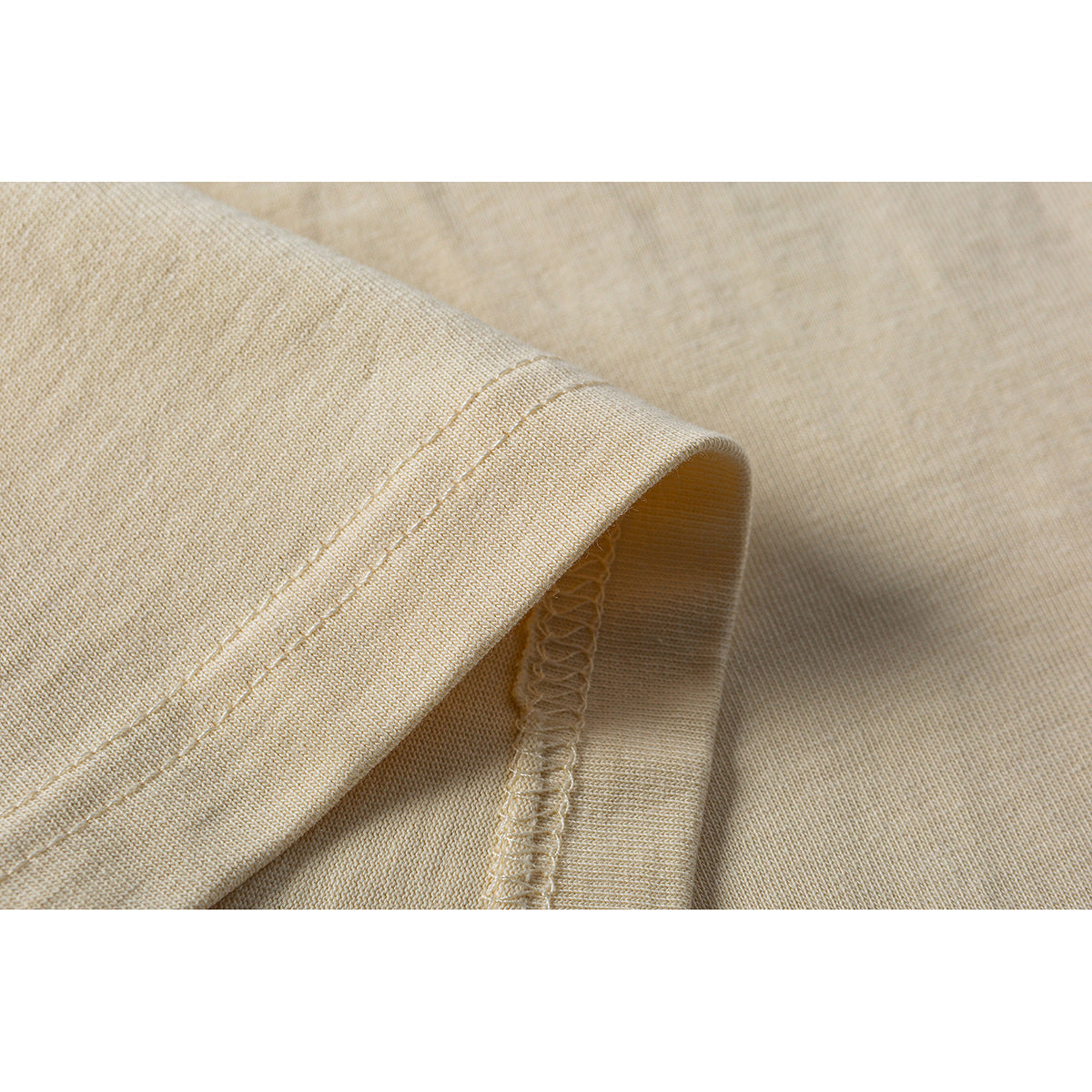 Close-up of the cream T-shirt's sleeve hem and overlocked seam stitching.