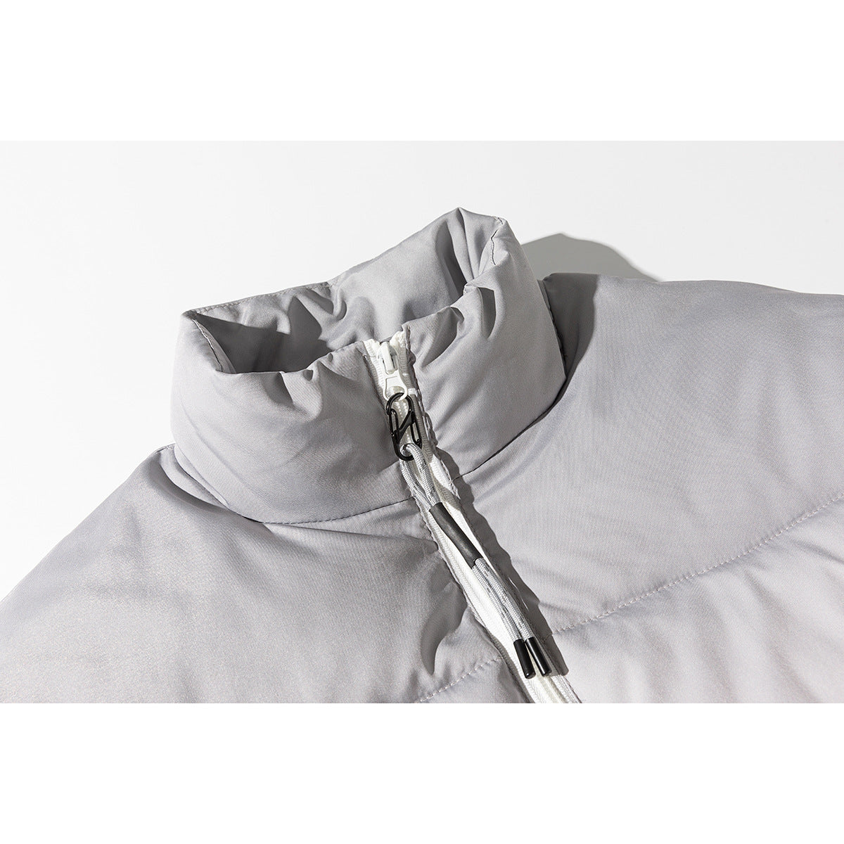 Close-up of a light gray padded jacket’s tall collar, white front zipper, and black zipper pull.