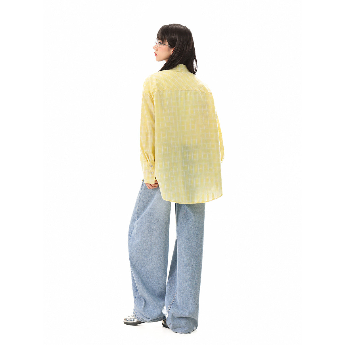 Rear view of a model wearing a loose yellow windowpane-check shirt with wide-leg blue jeans.