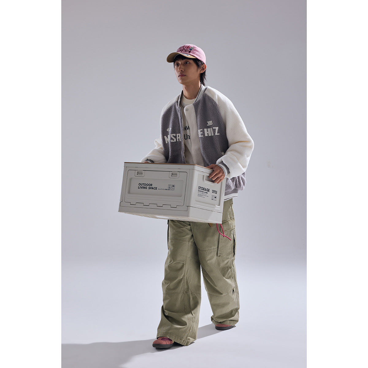 Model wearing a gray-and-white color-block fleece varsity jacket while holding a storage box; front view partly obscured.
