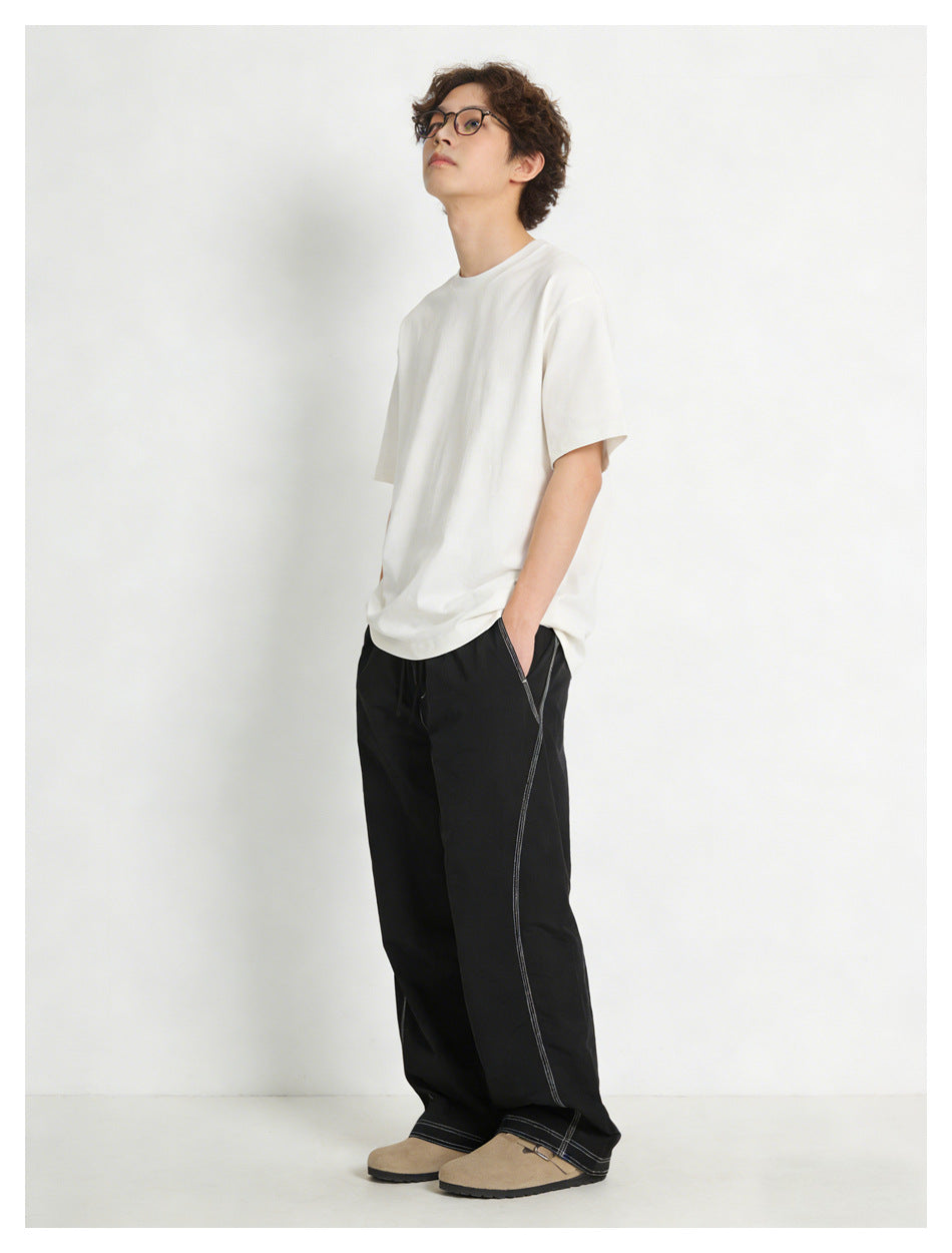 Model wearing black wide-leg pants with white contrast stitching and a white T-shirt.