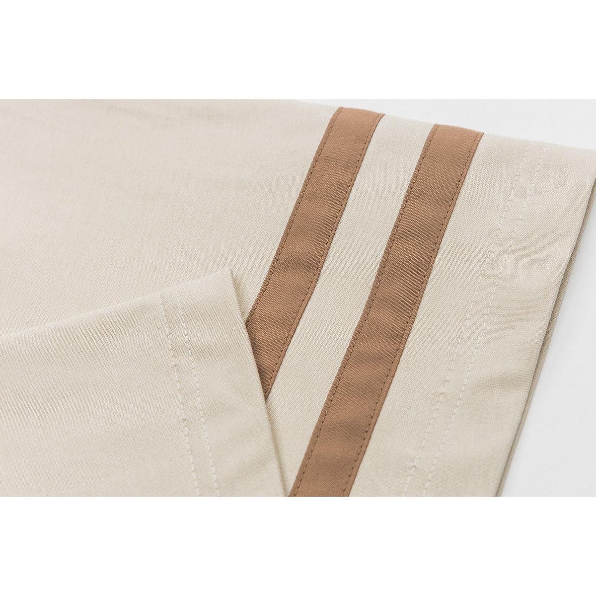 Close-up of two brown stripes and stitching on the sleeve of a cream T-shirt.