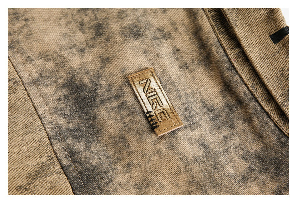Close-up of mottled tan fabric with a stitched rectangular label featuring stylized lettering.