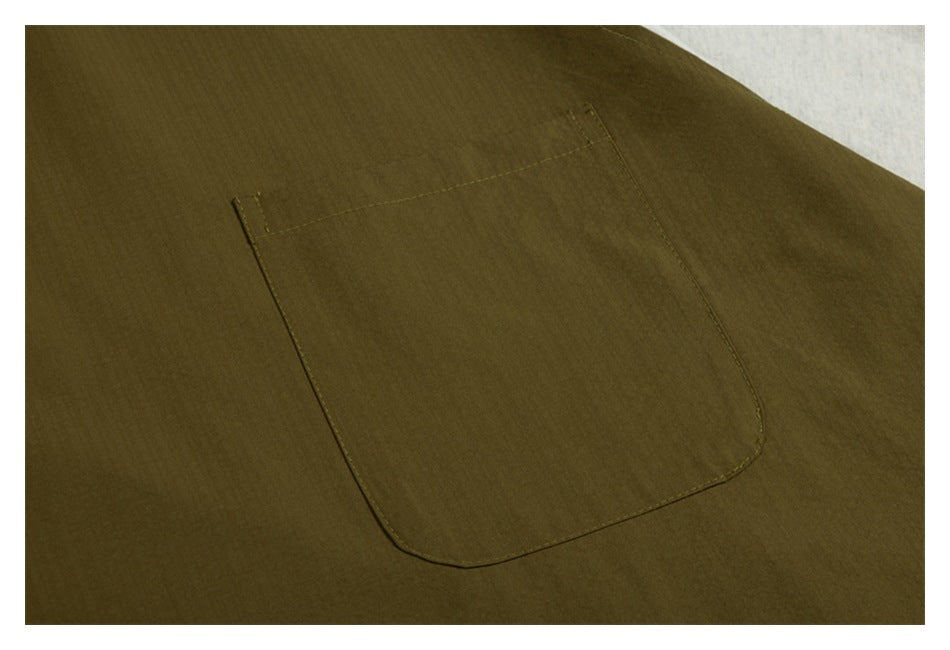 Close-up of an olive-brown garment with a large rectangular patch pocket and visible stitching.