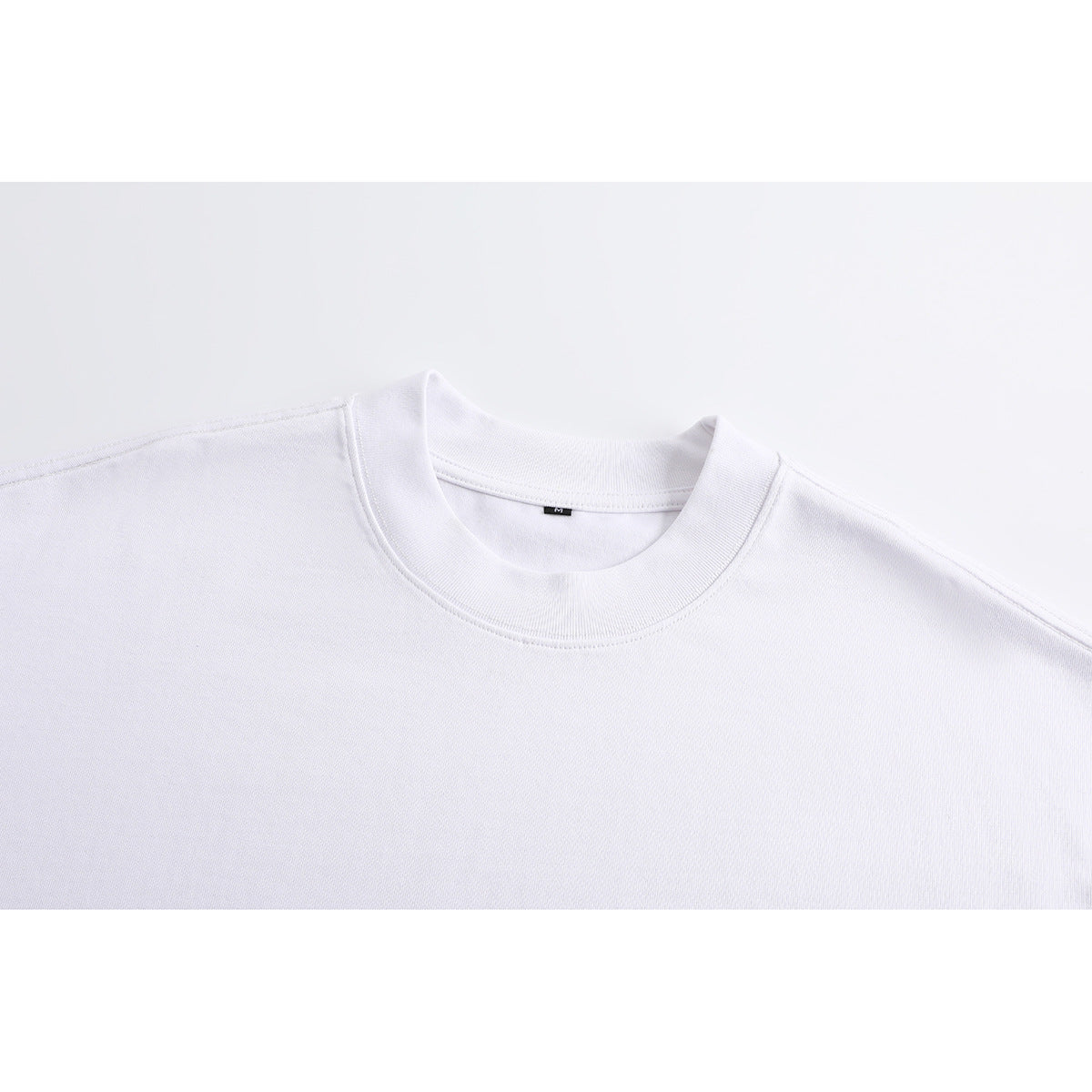 Close-up of a plain white T-shirt's ribbed crew neck and shoulder seams, with a small M size tag.