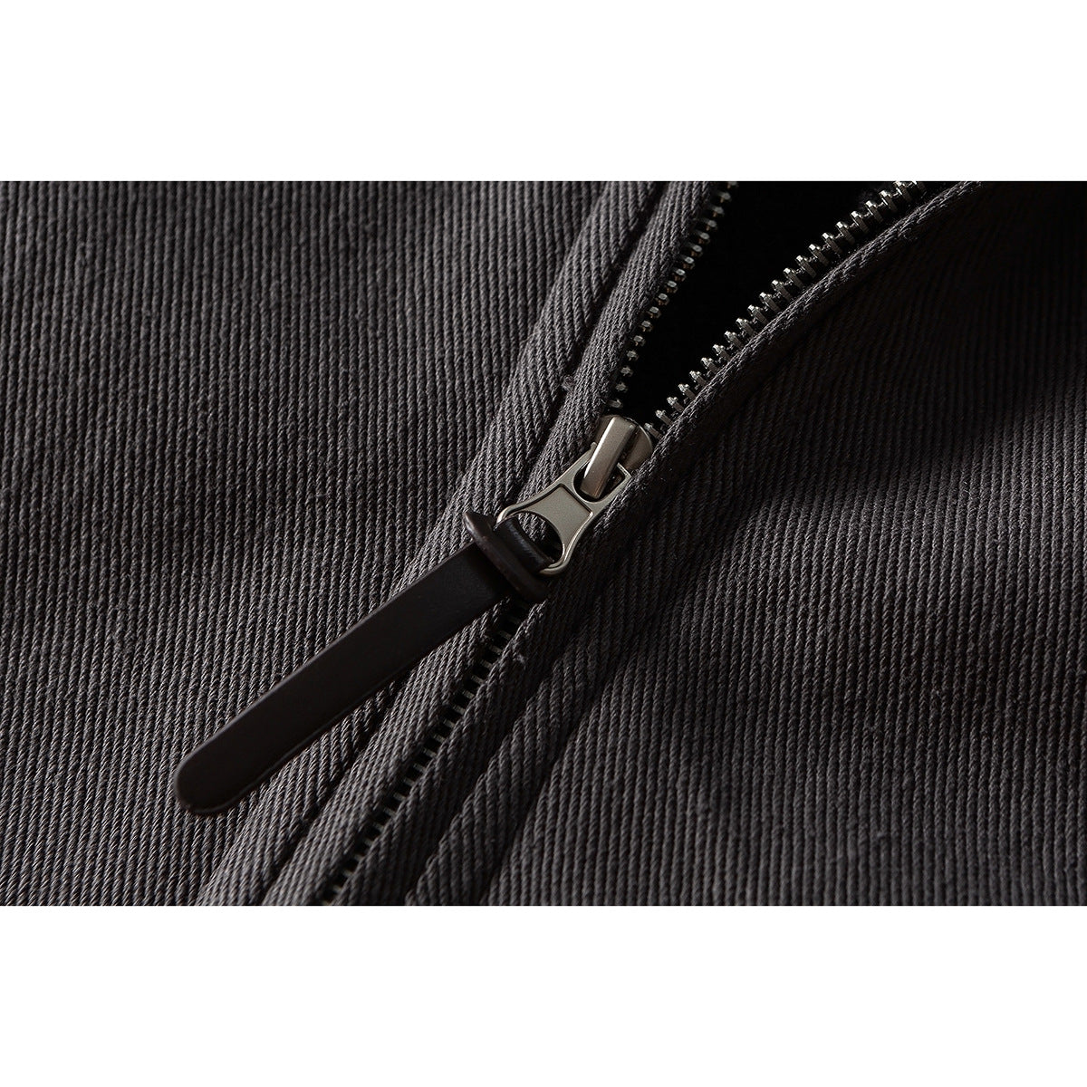 Close-up of a metal zipper and long black pull on charcoal fabric.